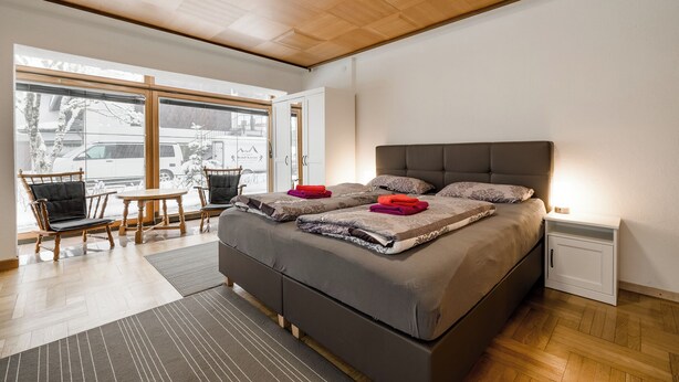 Een moderne slaapkamer met een groot bed, een houten plafond en uitzicht op buiten.