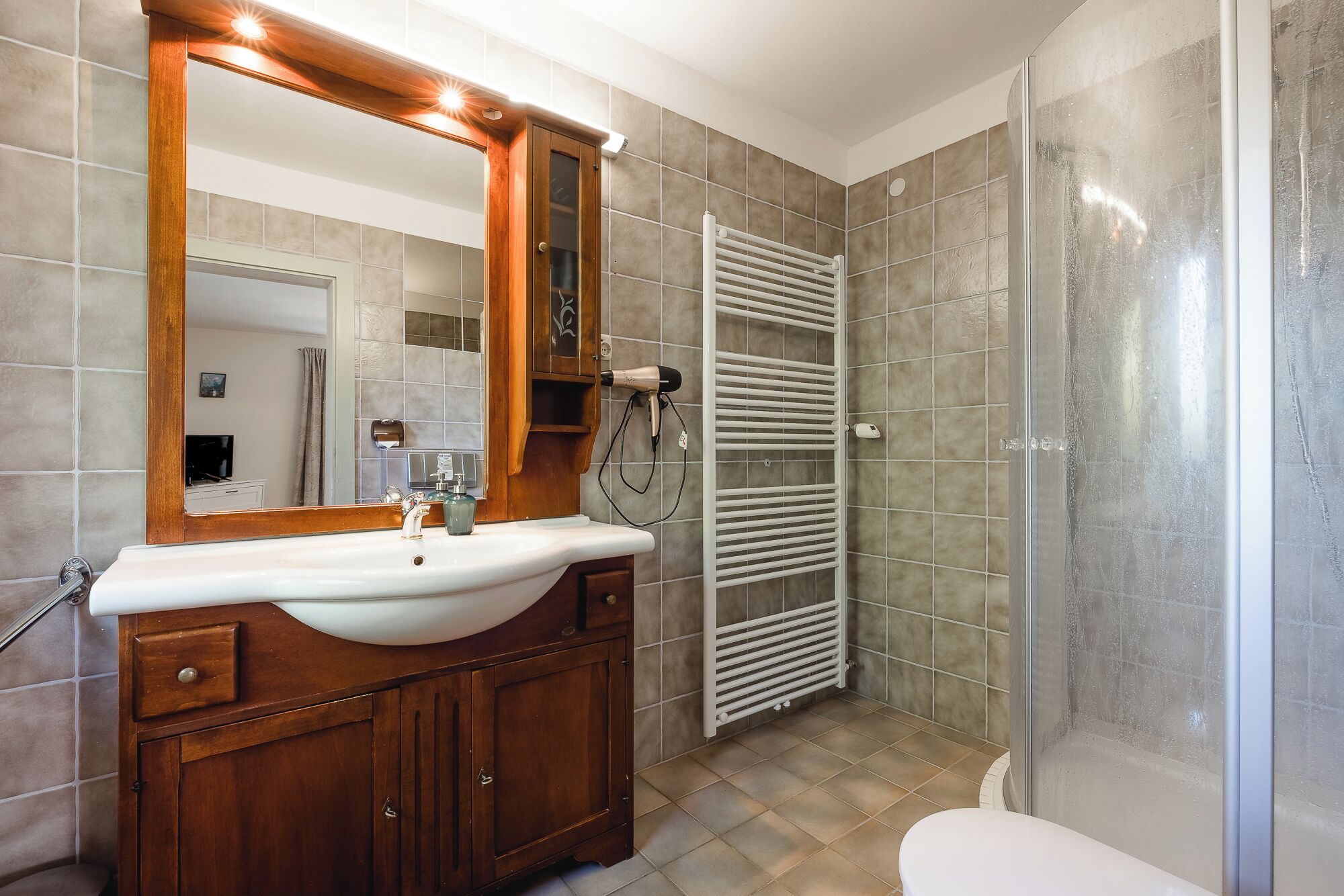 Une salle de bain avec un meuble-lavabo en bois, un lavabo blanc, un miroir, un porte-serviettes et un espace douche.