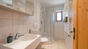 Een moderne badkamer met een groot, wit bad, een douche met glazen wand en een toilet.