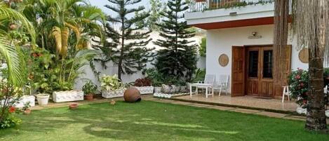 A well-maintained garden with a variety of plants and a lawn. There are outdoor seating arrangements and a door leading to the building.