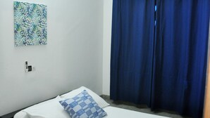 Uma cama de solteiro com roupa de cama branca, um travesseiro azul e um ar condicionado fixado na parede.