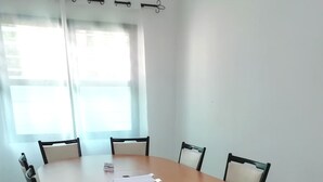 Uma sala de conferência com uma mesa redonda, seis cadeiras e uma janela com cortinas.