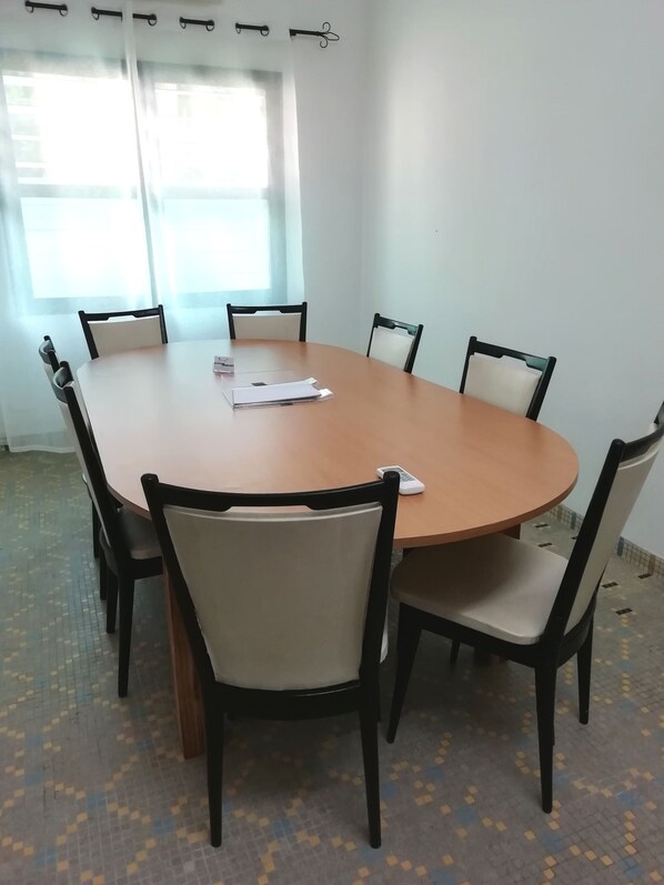 Un salón de conferencias con una mesa redonda, seis sillas y un ventanal con cortinas.
