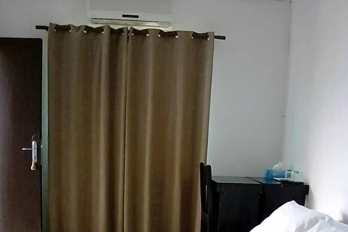 A hotel room with a bed, a desk, and a curtain.