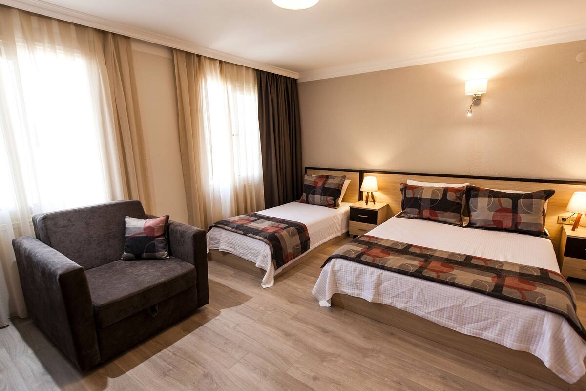 A hotel room with two beds, a sofa, and a nightstand with a lamp.