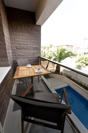 A balcony with a wooden table and chairs, a small pool, and a view of palm trees and buildings.