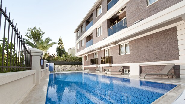A swimming pool adjacent to a multi-story building with balconies and a gated entrance. - Atrium Apart Hotel (Cesme)