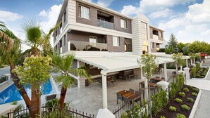 A modern multi-story hotel with a covered outdoor area, a swimming pool, and lush landscaping. - Atrium Apart Hotel (Cesme)