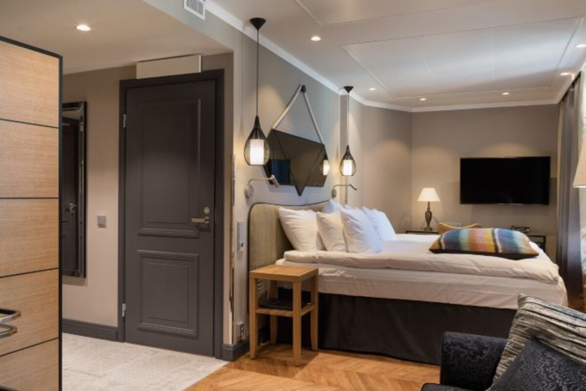 Een moderne hotelkamer met een bed, nachtkastje, lamp en een aan de muur bevestigde televisie.