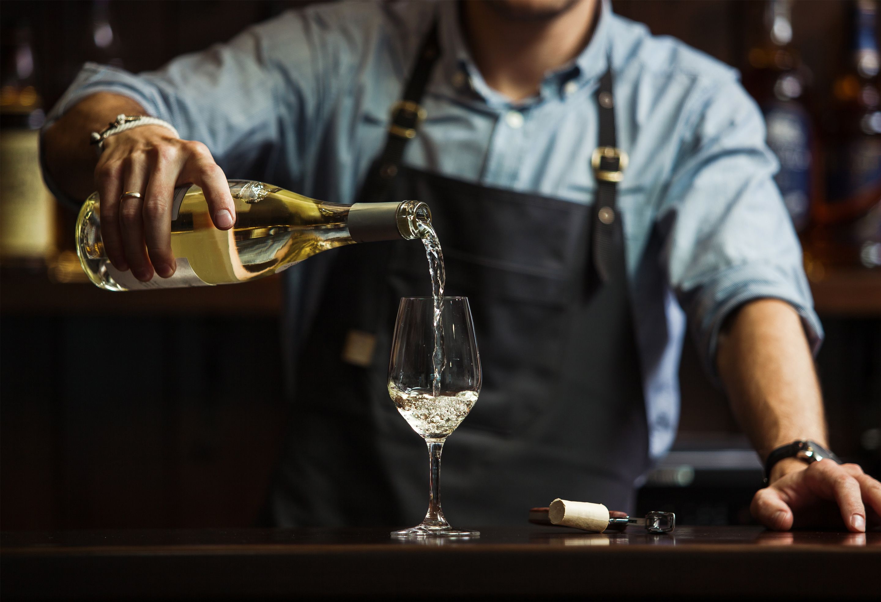 A person pouring a clear liquid from a bottle into a glass.