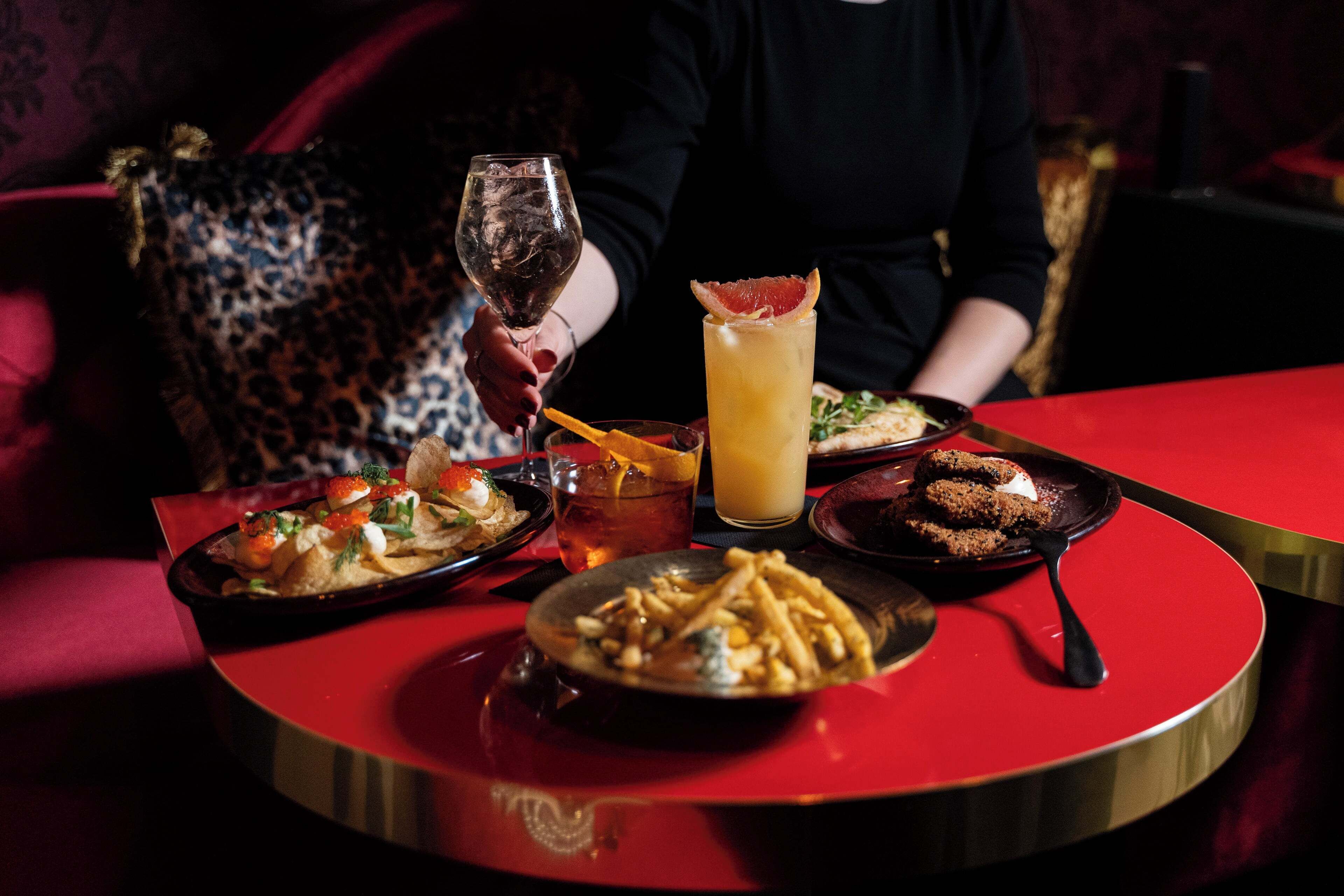 Una mesa de comedor con varios platos, una copa de vino y un cóctel.