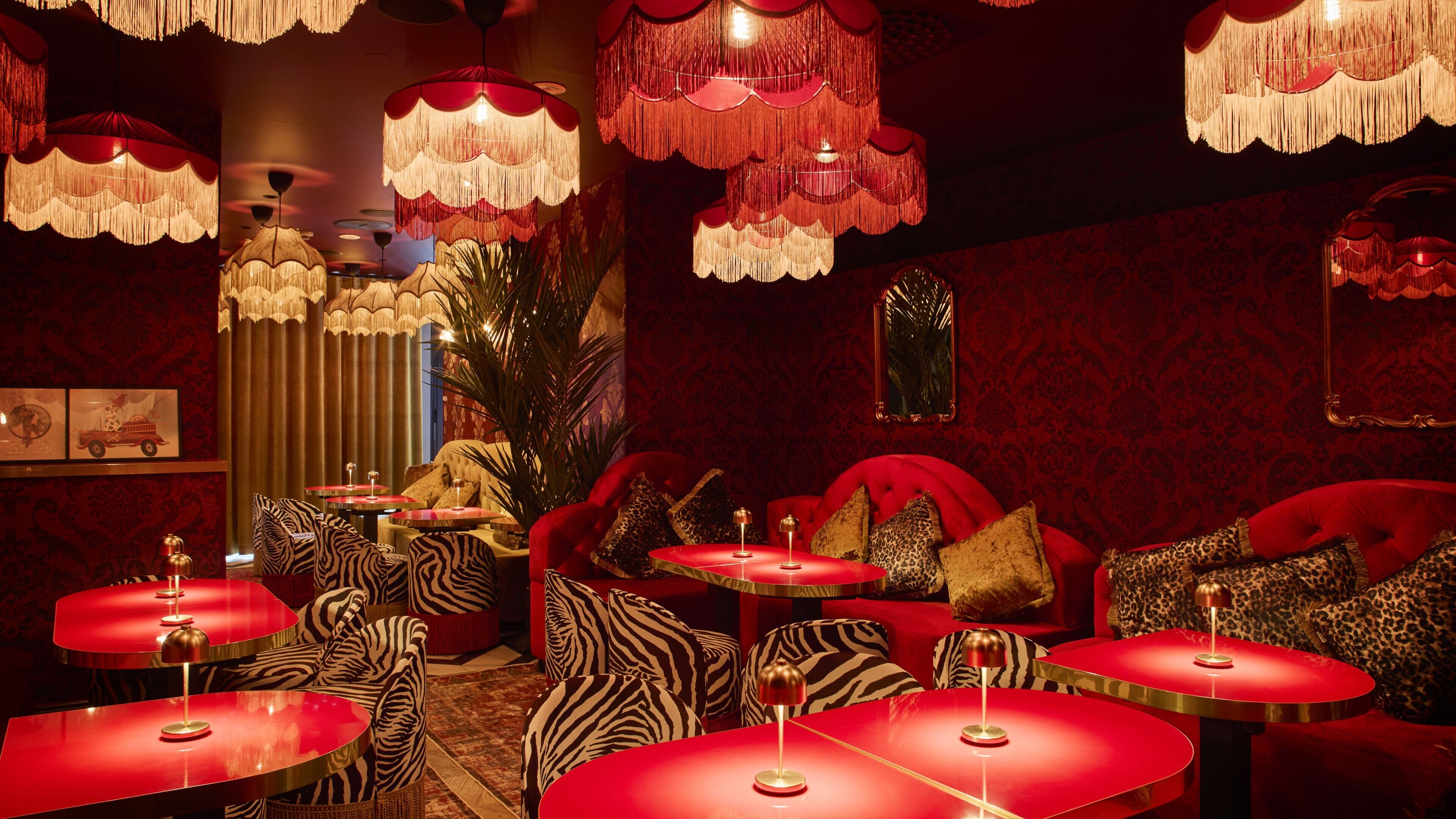 A room with red furniture, zebra-patterned chairs, and multiple red tables with lamps.