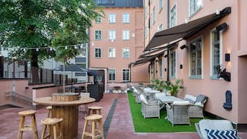 Une terrasse extérieure avec une table ronde en bois, des tabourets de bar et des meubles en osier.