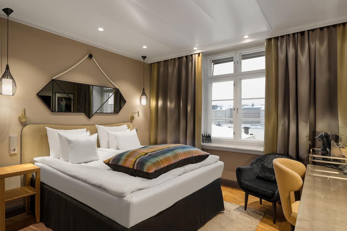Une chambre d’hôtel moderne, dotée d’un grand lit, d’un bureau et offrant une vue sur la ville par la fenêtre.