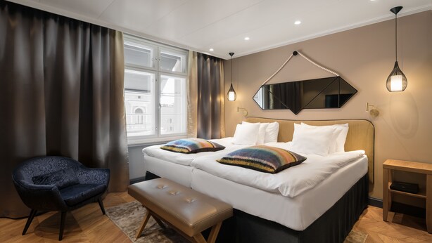 Une chambre d’hôtel moderne avec un lit double, une banquette, une chaise et une grande fenêtre.