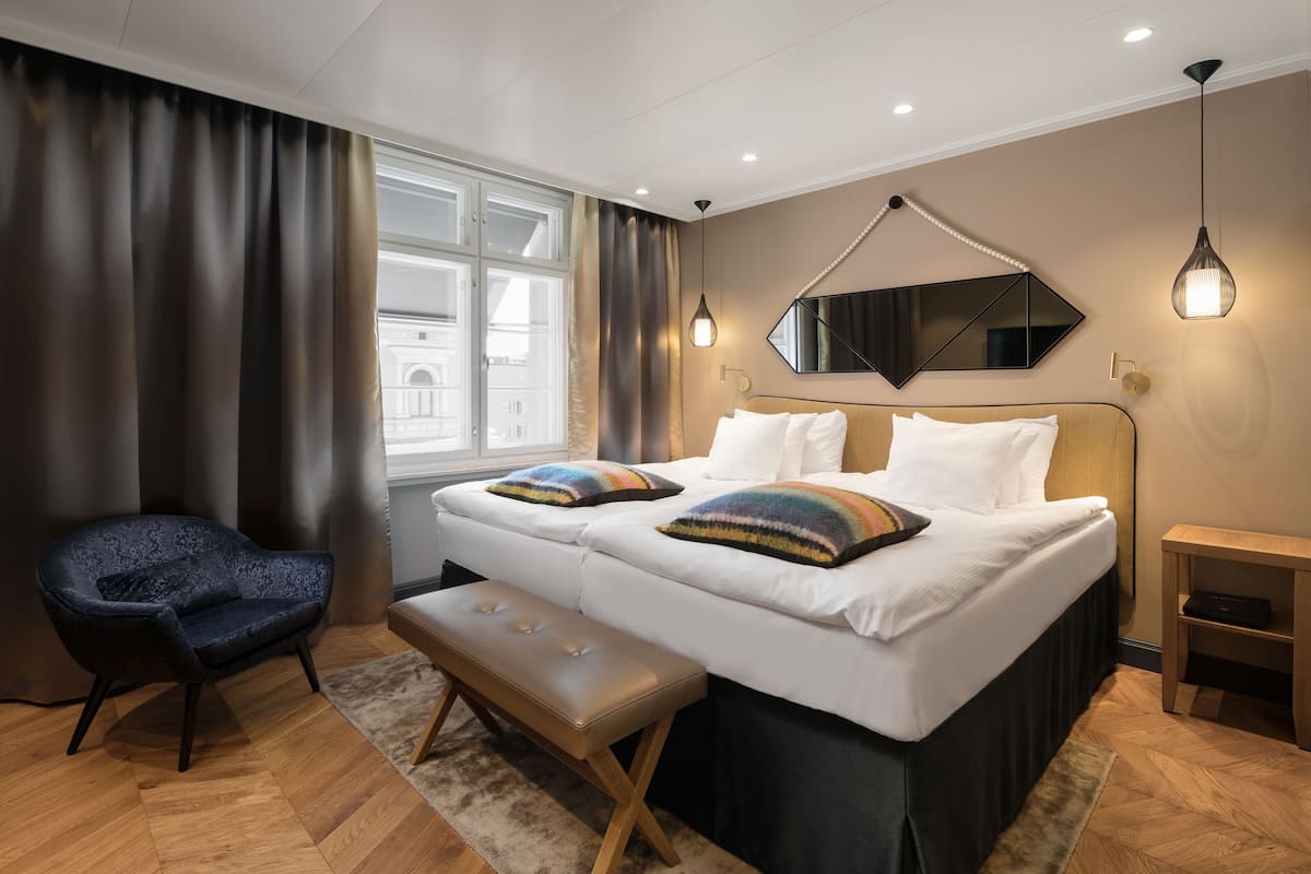 Une chambre d’hôtel moderne avec un lit double, une banquette, une chaise et une grande fenêtre.