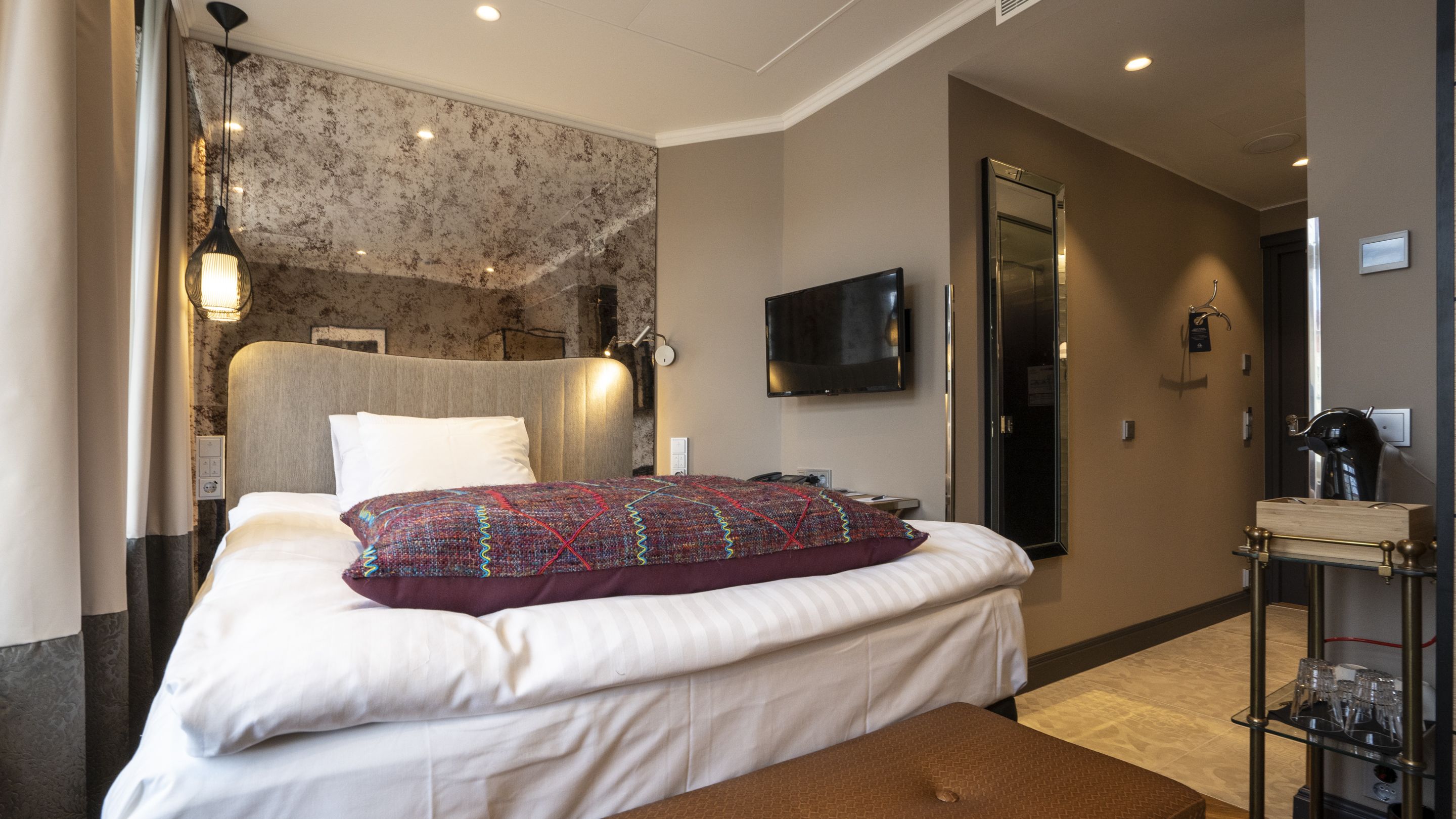 Una habitación de hotel con cama, televisión, espejo y minibar.