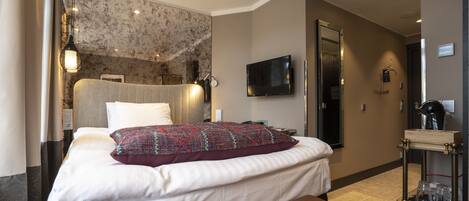 Una habitación de hotel con cama, televisión, espejo y minibar.