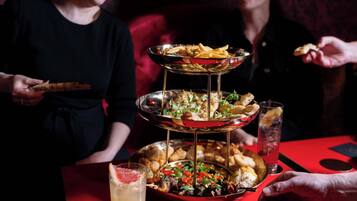 A multi-tiered serving tray with various food items and a drink on a red table.