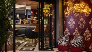 Un espace bar agrémenté d’un panneau néon sur lequel on peut lire : « C’EST L’HEURE DU COCKTAIL ! », et de chaises à motifs zébrés à l’extérieur.