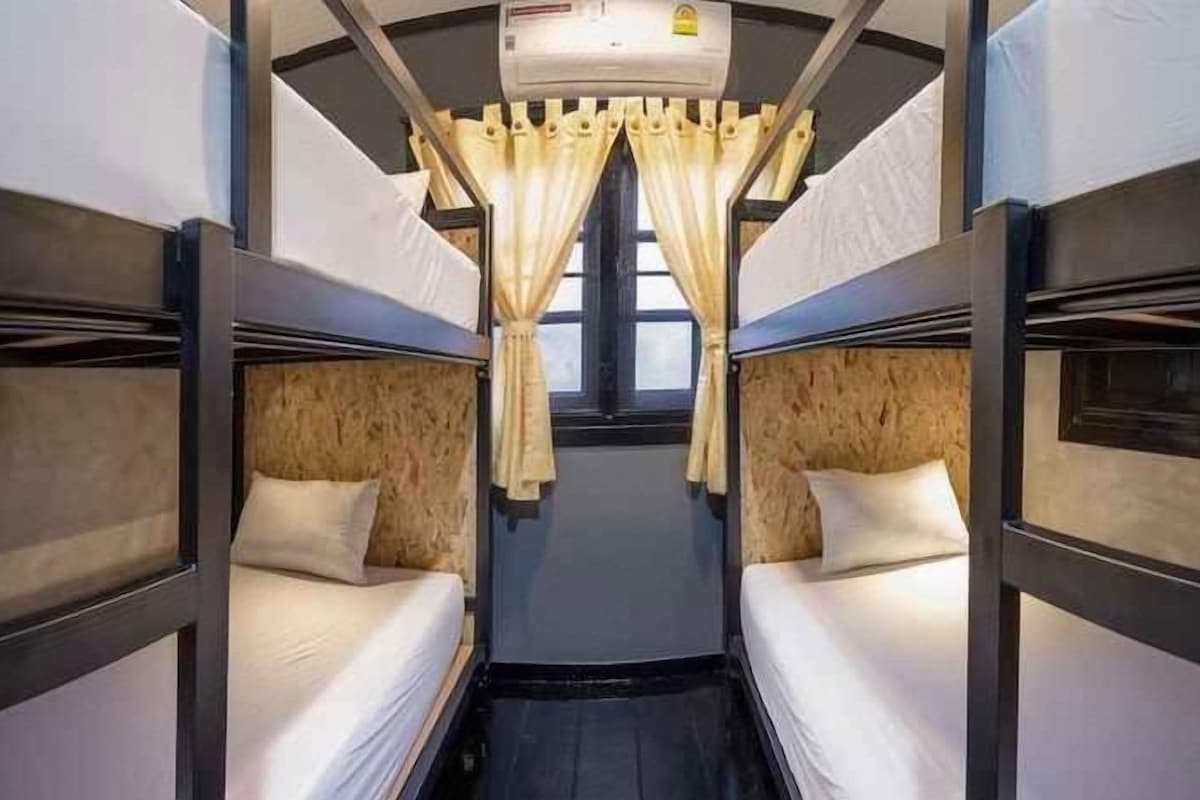 A train compartment with bunk beds, a window with curtains, and an air conditioning unit.