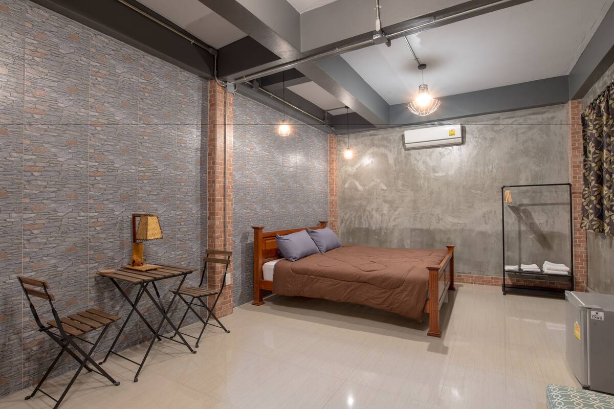Une chambre à coucher avec un lit, un bureau avec une lampe, deux chaises, une armoire et une petite table.