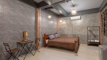 A bedroom with a bed, a desk with a lamp, two chairs, a wardrobe, and a small table.