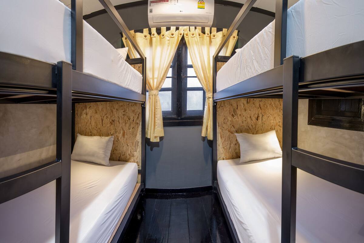 Un compartiment de train avec des lits superposés, une fenêtre avec des rideaux et un appareil de climatisation.