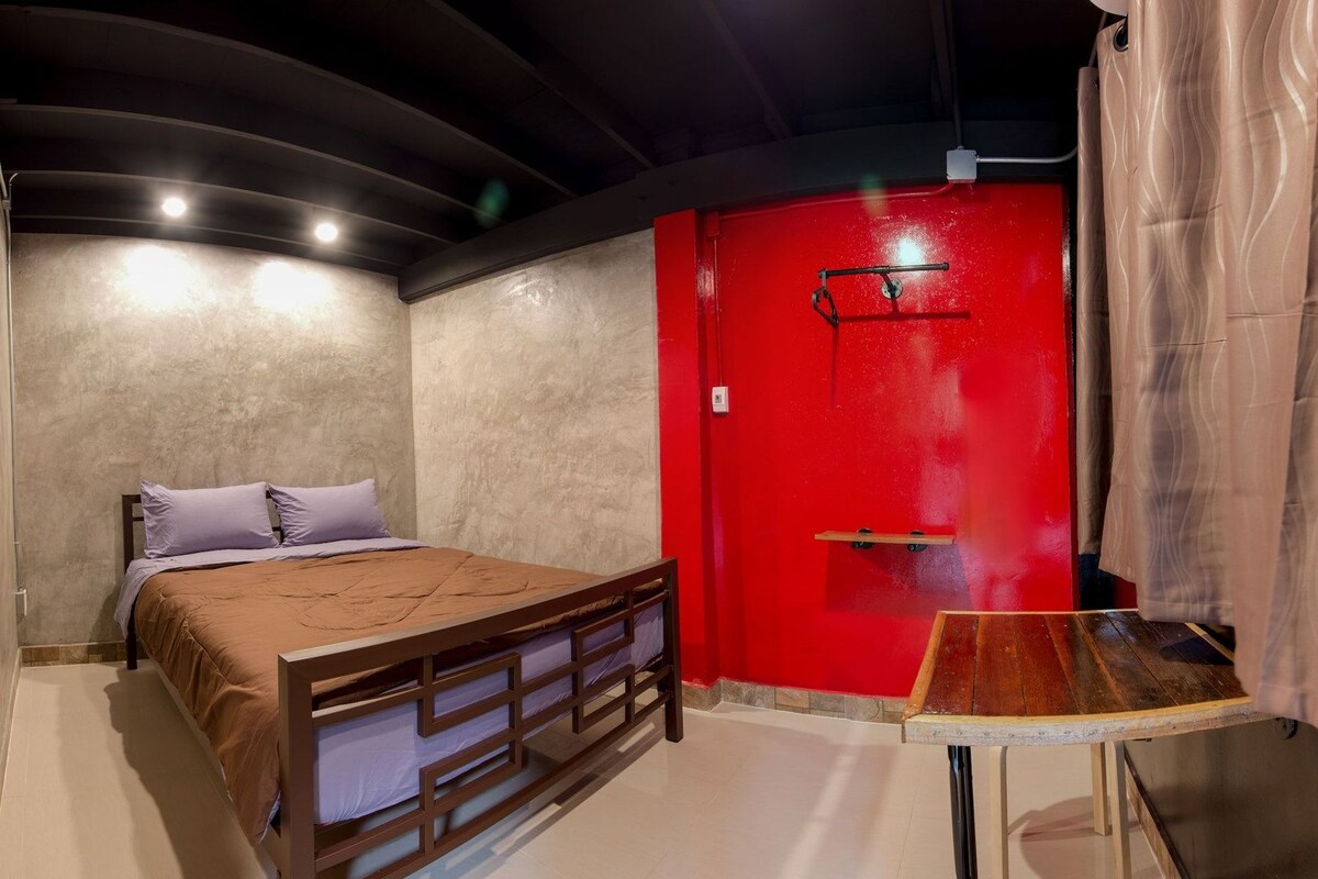 A bedroom with a bed, a red door, and a small table.