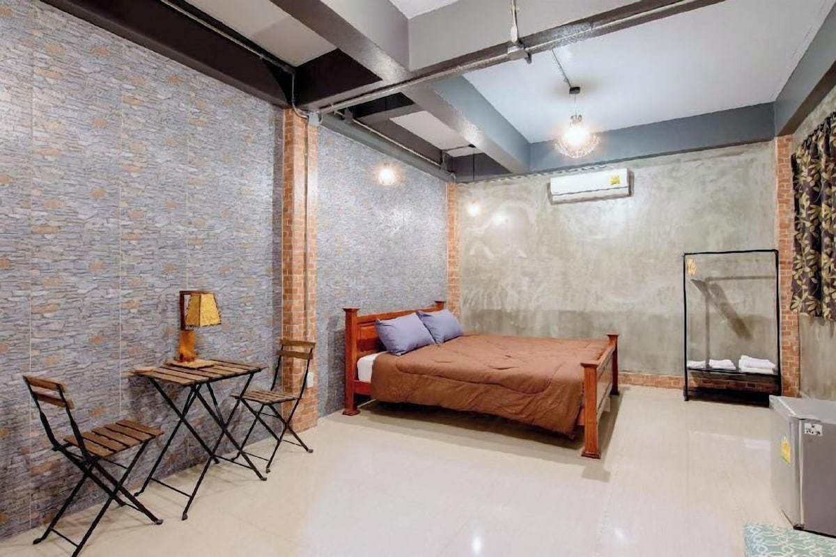 A bedroom with a bed, a small table with chairs, a lamp, and a wardrobe.