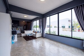 A modern living room with a sofa, a coffee table, and a large window with curtains. - Mango Home 102 (Hua Hin)