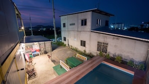 A residential building with a rooftop pool, a covered patio area with seating, and a view of the surrounding neighborhood at dusk. - Mango Home 102 (Hua Hin)