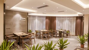 Un espace de restauration moderne avec des tables et des chaises en bois, des plantes en pot et une grande fenêtre agrémentée de rideaux.