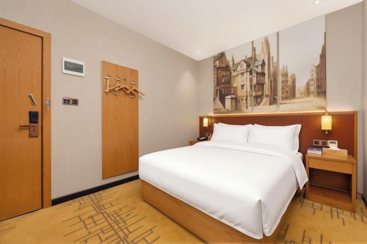 Une chambre d’hôtel avec un grand lit, une armoire, un tableau au mur et une table de chevet avec une lampe.