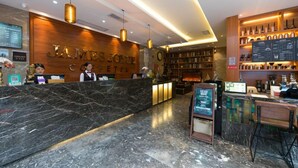 Un hall d’accueil d’hôtel avec un comptoir en marbre, un bureau d’accueil, un coin salon doté d’une cheminée et une bibliothèque remplie de livres.