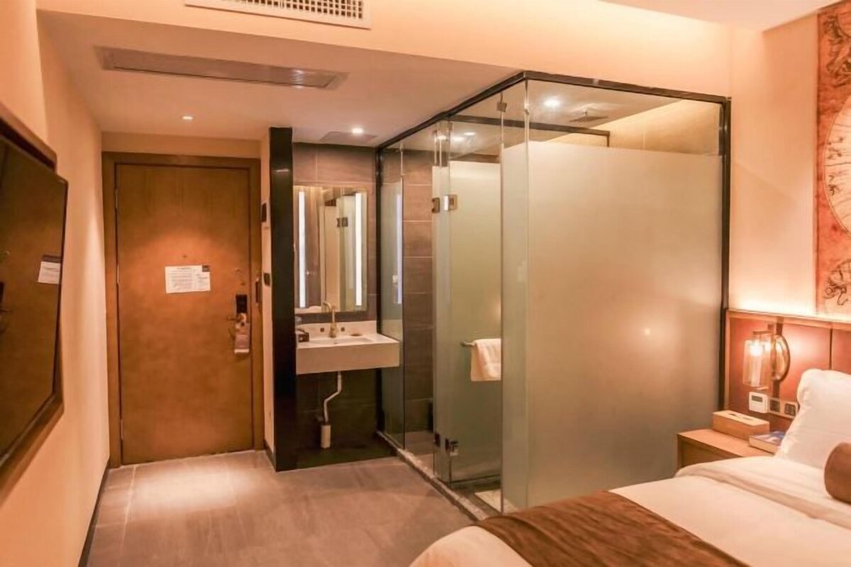 Ein Hotelzimmer mit Bett, Badezimmer mit Duschkabine, Waschbecken und Nachttisch mit Lampe.