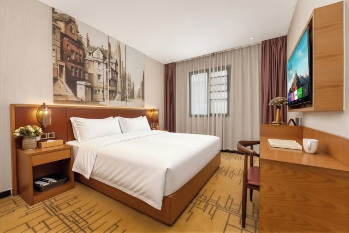 Une chambre d’hôtel avec un grand lit, un bureau, une télévision et un tableau au mur.