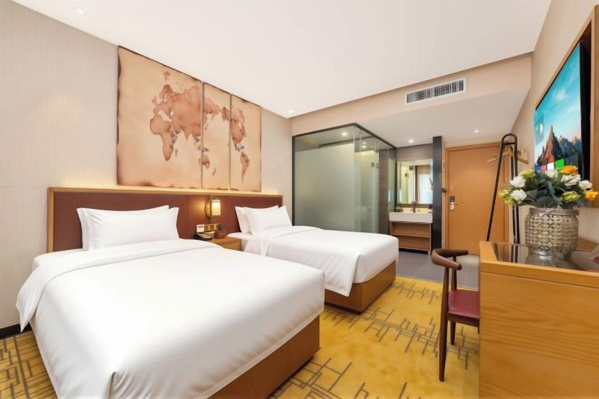 Ein Hotelzimmer mit zwei Betten, einem Schreibtisch, einem Stuhl und einer großen Weltkarte an der Wand, sowie einem Fernseher.