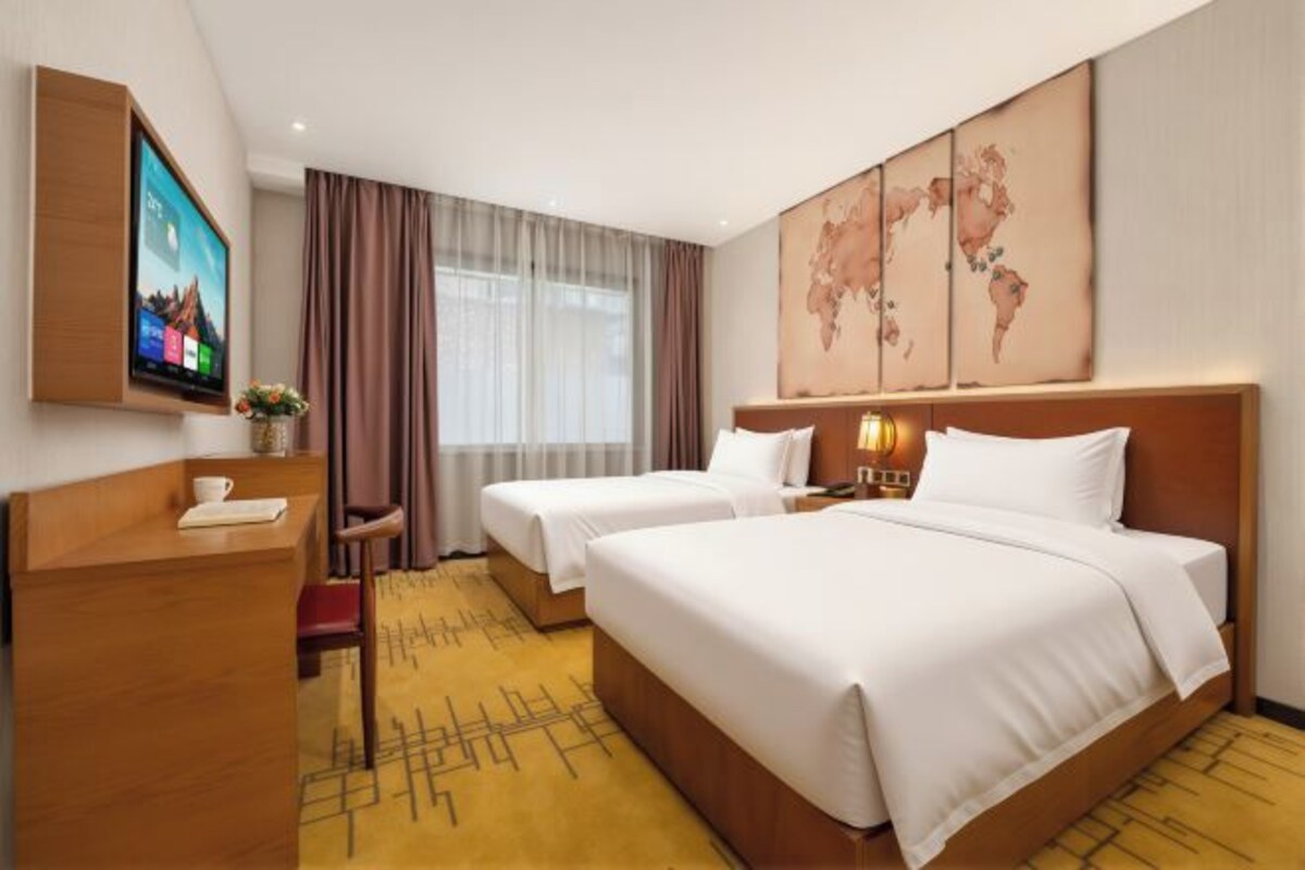 Une chambre d’hôtel avec deux lits, un bureau, une télévision et une grande fenêtre avec des rideaux.