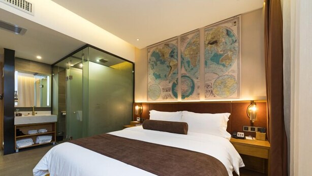 Une chambre d’hôtel dotée d’un grand lit, d’une douche séparée par des parois en verre, d’une coiffeuse en bois avec un miroir et d’une grande carte du monde accrochée au mur.