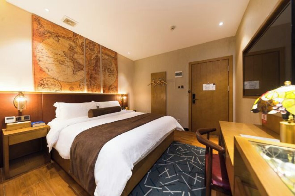 Une chambre d’hôtel avec un grand lit, un bureau avec une lampe, une carte accrochée au mur et une porte en bois.