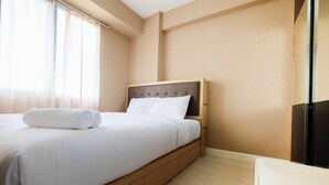 A neatly made bed with white linens and a rolled towel, a wooden headboard, and a small bedside table. - Homely 2 Bedroom at Bassura City Apartment By Travelio (Jakarta)