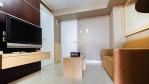 A modern living room with a flat-screen TV, a small wooden table, and a patterned sofa. - Homely 2 Bedroom at Bassura City Apartment By Travelio (Jakarta)
