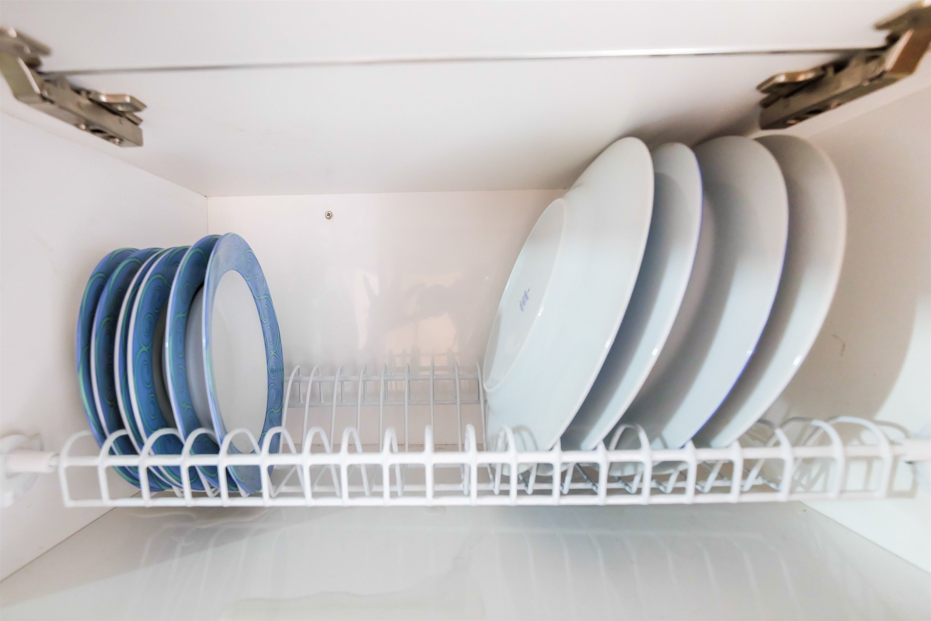 A white shelf with a white rack holding plates and bowls.