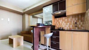 A modern kitchen with wooden cabinets, a built-in stove, and a bar stool. - Homely 2 Bedroom at Bassura City Apartment By Travelio (Jakarta)