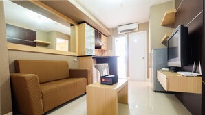 A modern living room with a sofa, a coffee table, a television, and a kitchenette area. - Homely 2 Bedroom at Bassura City Apartment By Travelio (Jakarta)