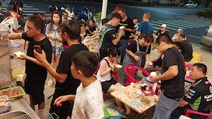 Un groupe de personnes s’est rassemblé autour d’un stand de nourriture équipé d’un gril, de tables et de chaises.