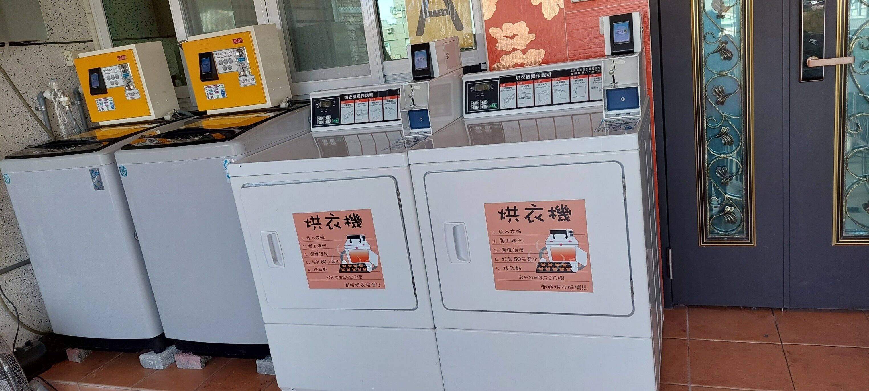 Une laverie équipée de plusieurs machines à laver et de plusieurs séchoirs, chacun étant doté d’un panneau de commande et d’une affiche indiquant les instructions.