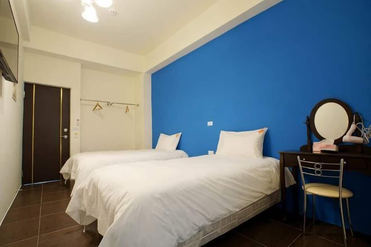 Een slaapkamer met twee bedden, een bureau met stoel, een spiegel en een blauwe accentmuur.