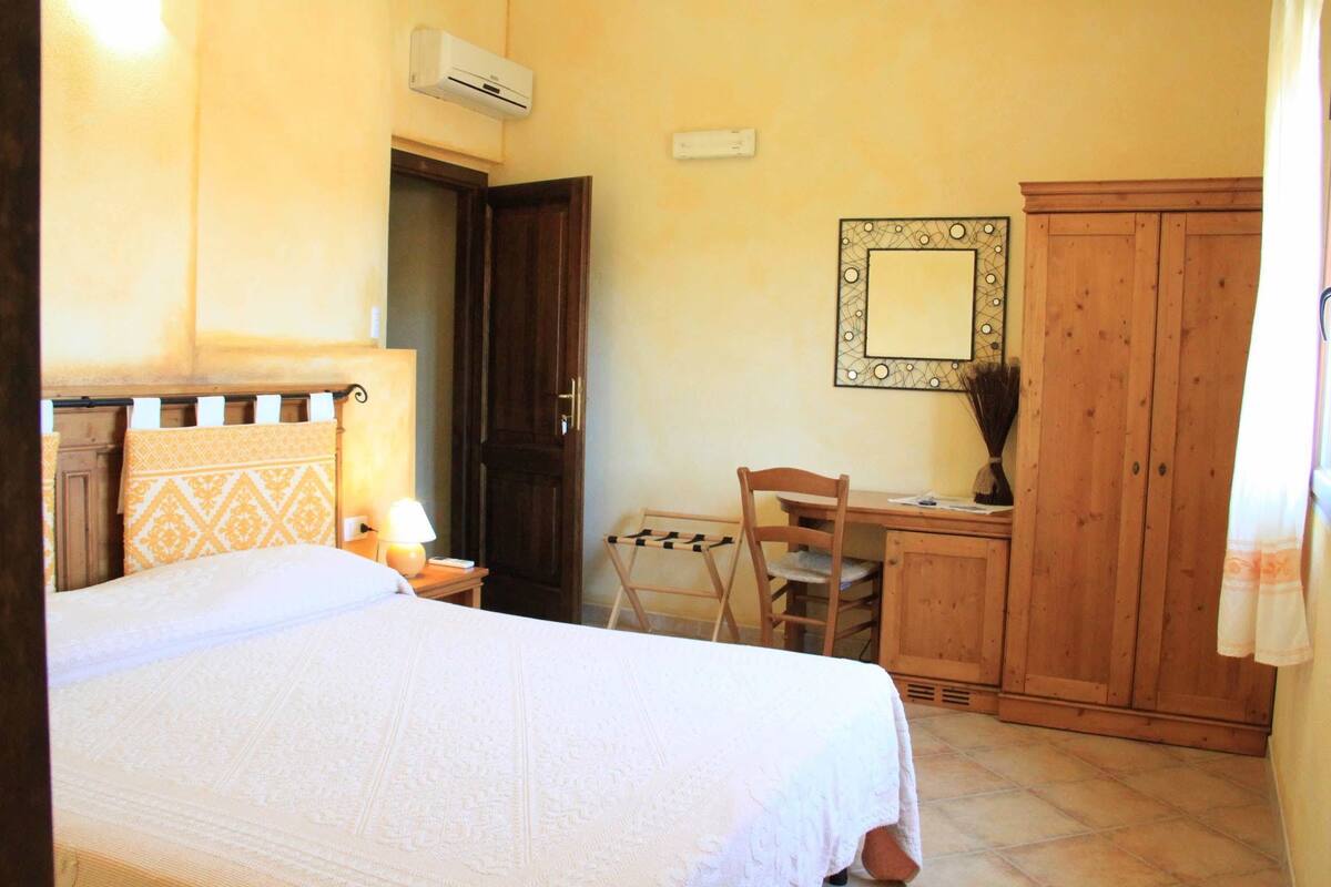 A bedroom with a bed, a desk, a chair, a wardrobe, and an air conditioning unit.